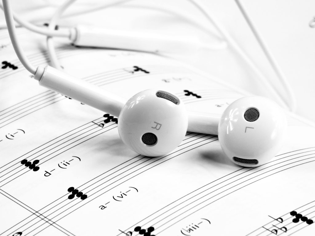 Close-up of white earphones resting on sheet music, emphasizing music and sound themes.