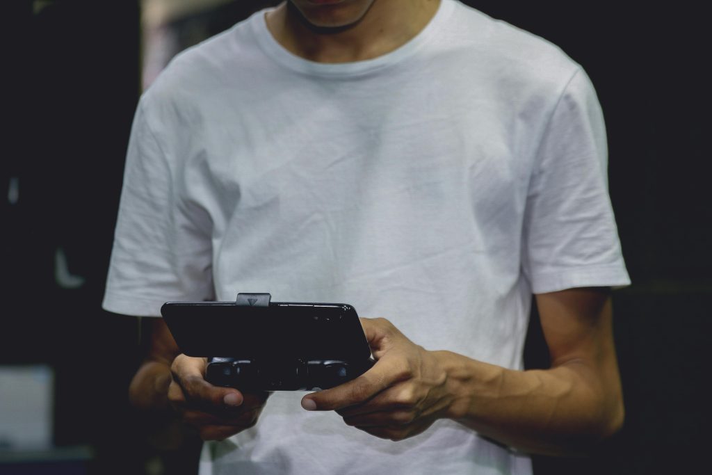 A young man in a white shirt using a smartphone game controller indoors.